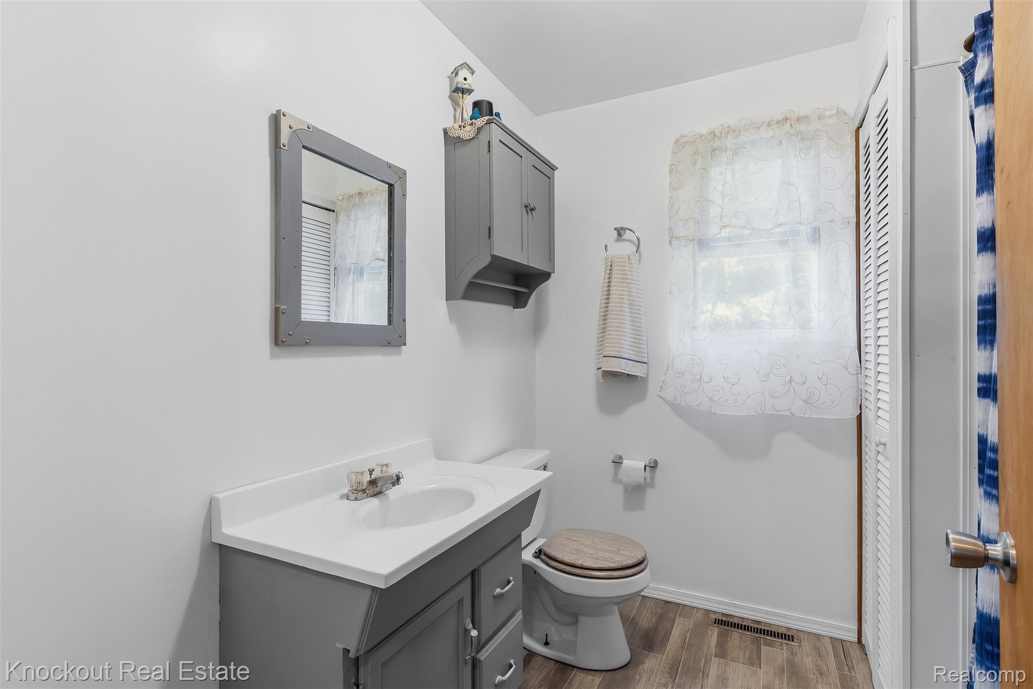 12845 Bueche Road Burt, MI 48417 - Photo 13 of 28 Bathroom featuring a vanity with a white countertop and gray cabinetry, wood-finish flooring, a window, and a built-in storage cabinet