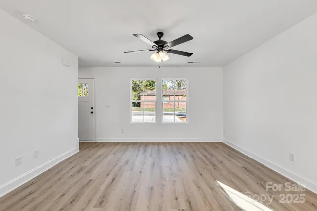 an empty room with wooden floor a ceiling fan and windows