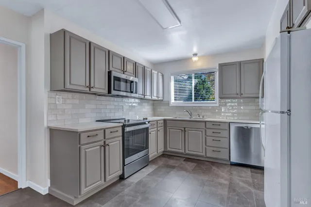 a kitchen with stainless steel appliances granite countertop a stove top oven a sink dishwasher and a refrigerator with wooden cabinets