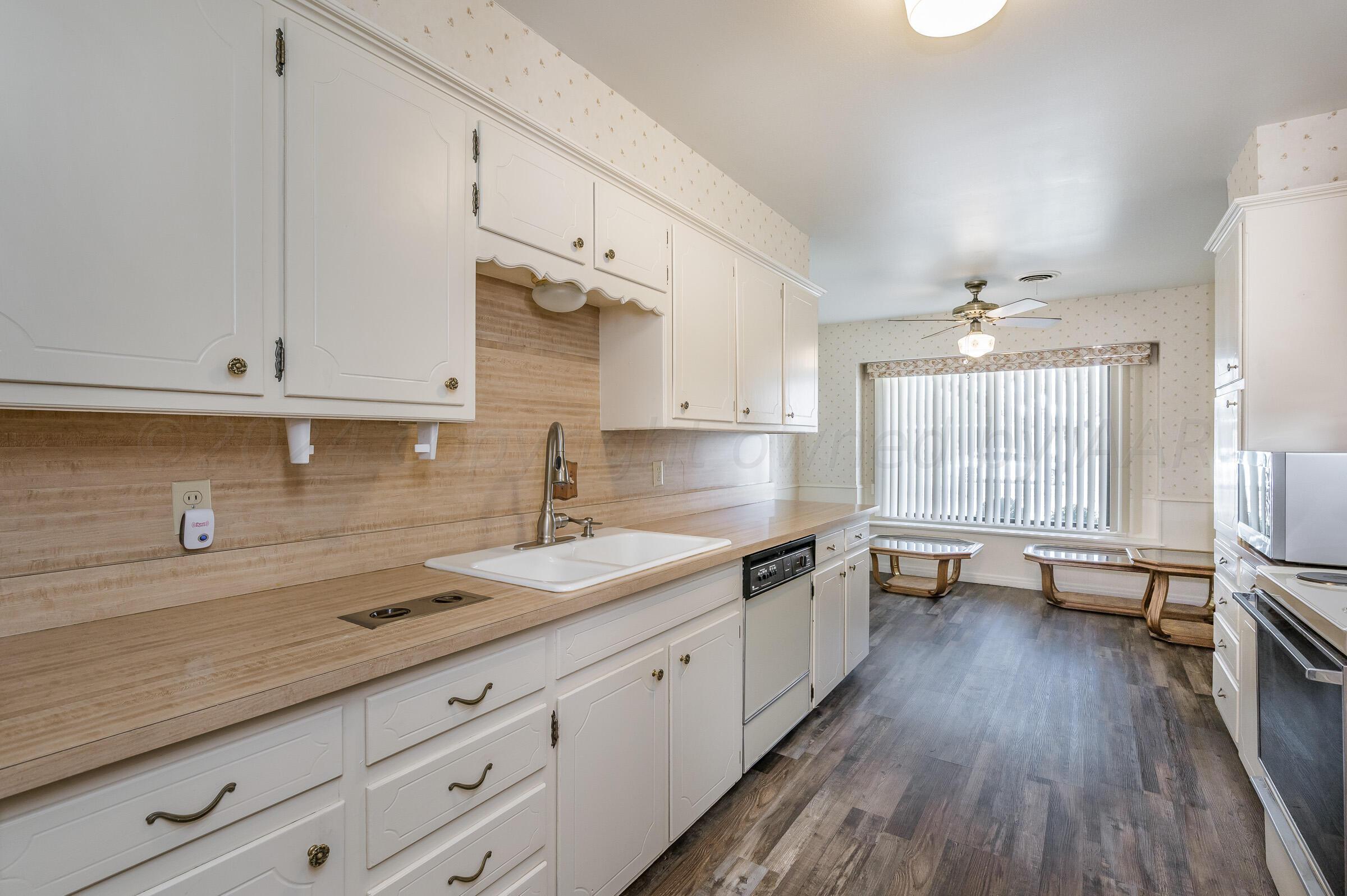 6113 Elmhurst Road Amarillo, TX 79106 - Photo 7 of 28 a kitchen with a sink dishwasher stove and white cabinets with wooden floor