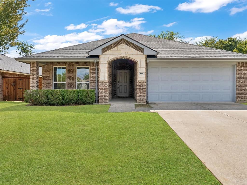 Ranch-style home with a front yard, brick siding, concrete driveway, and an attached garage