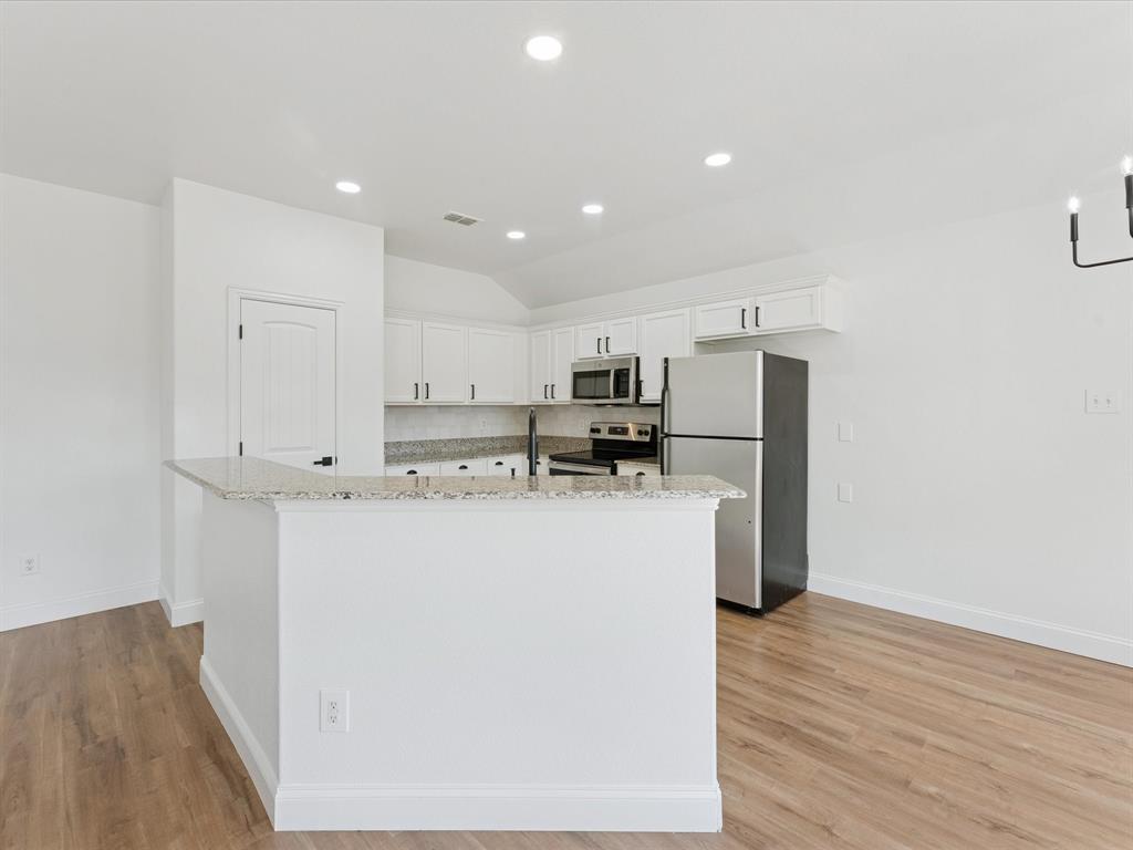 810 Ranch Road Dallas, TX 75253 - Photo 17 of 28 Kitchen with light stone countertops, white cabinetry, appliances with stainless steel finishes, lofted ceiling, and an island with sink
