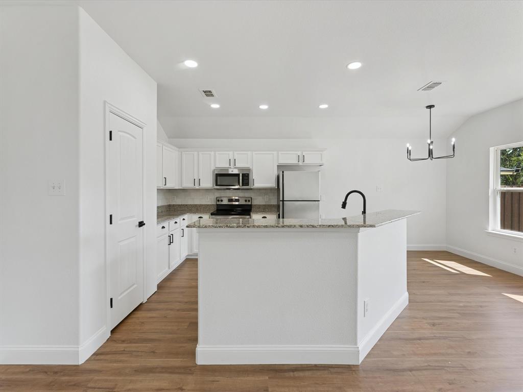 810 Ranch Road Dallas, TX 75253 - Photo 18 of 28 Kitchen featuring pendant lighting, white cabinets, light stone counters, appliances with stainless steel finishes, and a center island with sink