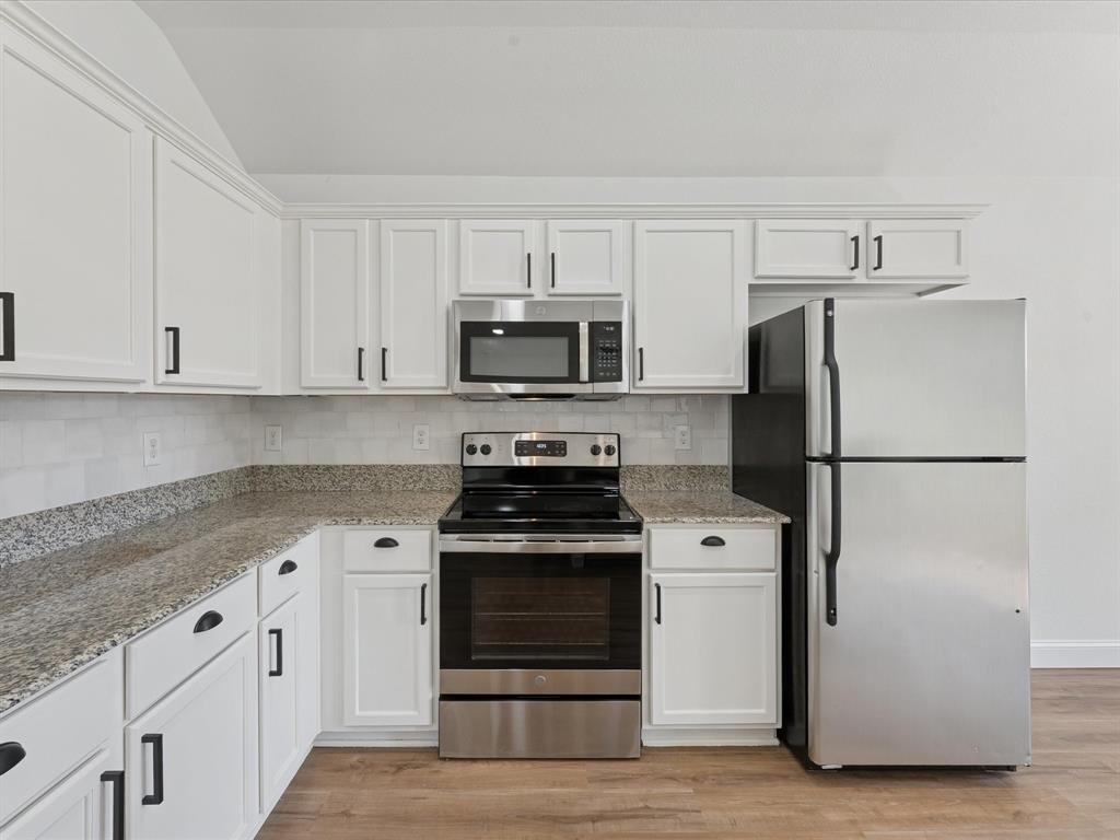 810 Ranch Road Dallas, TX 75253 - Photo 19 of 28 Kitchen featuring stainless steel appliances, white cabinetry, light stone countertops, and vaulted ceiling
