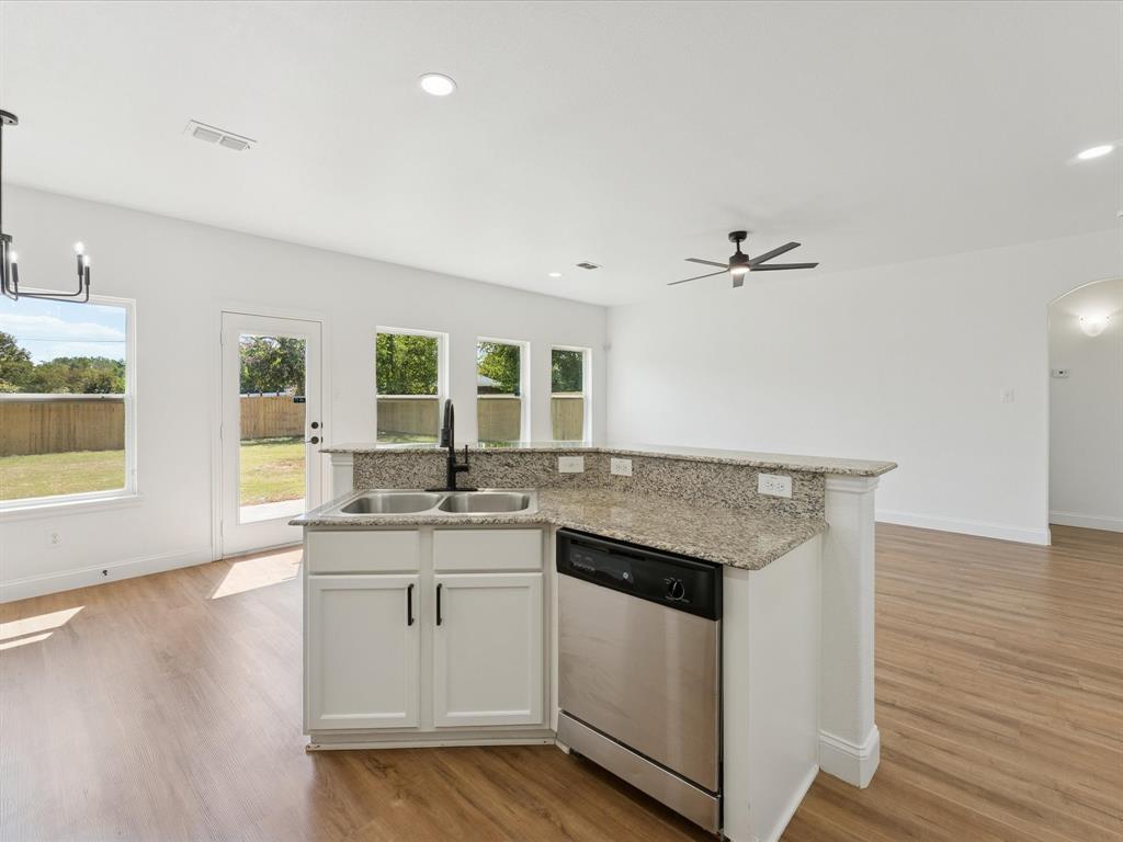 810 Ranch Road Dallas, TX 75253 - Photo 28 of 28 Kitchen featuring white cabinets, an island with sink, arched walkways, stainless steel dishwasher, and open floor plan