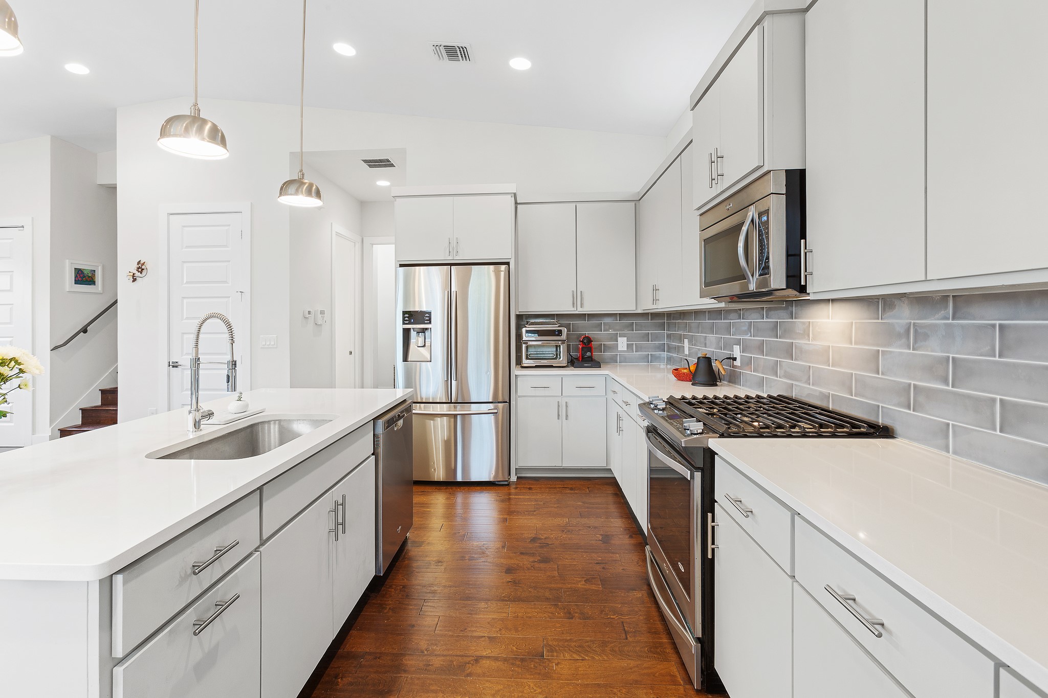 3101 Sunnylawn Circle, Unit B Austin, TX 78723 - Photo 7 of 32 Kitchen featuring appliances with stainless steel finishes, a kitchen island with sink, tasteful backsplash, pendant lighting, and white cabinetry