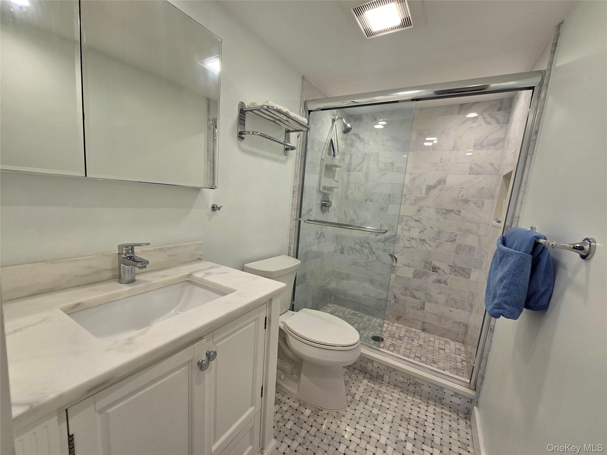 585 Dune Road, Unit L10 Westhampton, NY 11978 - Photo 15 of 25 Bathroom featuring a single vanity with a white countertop and integrated sink, a mirrored medicine cabinet, a walk-in shower with a glass enclosure and marbled wall tiles, and mosaic tile flooring