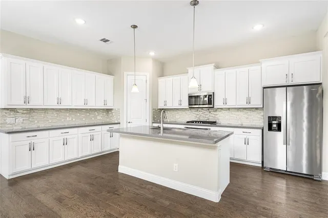 a kitchen with stainless steel appliances kitchen island granite countertop a refrigerator a sink dishwasher a stove and white cabinets with wooden floor