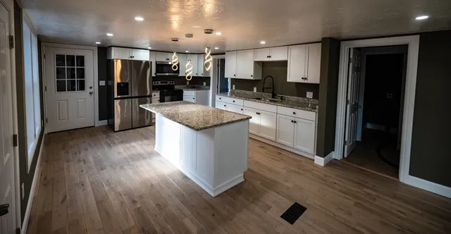 a kitchen with stainless steel appliances granite countertop a refrigerator a sink dishwasher a stove and a microwave oven on the wooden floor