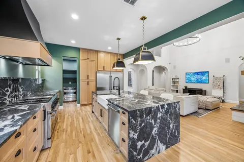 a kitchen with stainless steel appliances kitchen island granite countertop a refrigerator a stove and a wooden floors