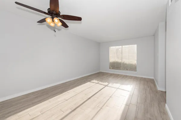 an empty room with wooden floor fan and windows