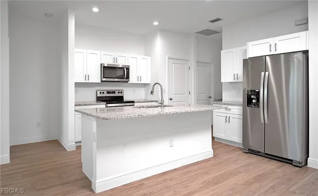 a kitchen with stainless steel appliances granite countertop a refrigerator a sink a stove a microwave and wooden floor