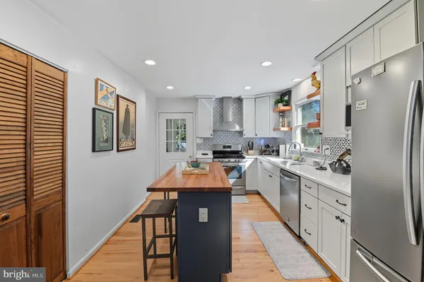 a large kitchen with stainless steel appliances granite countertop a refrigerator a sink dishwasher a stove and white cabinets with wooden floor