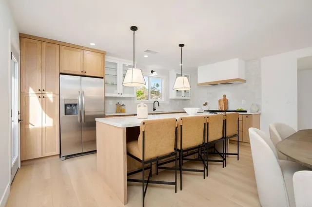 a kitchen with stainless steel appliances a refrigerator a sink a stove and chairs with wooden floor