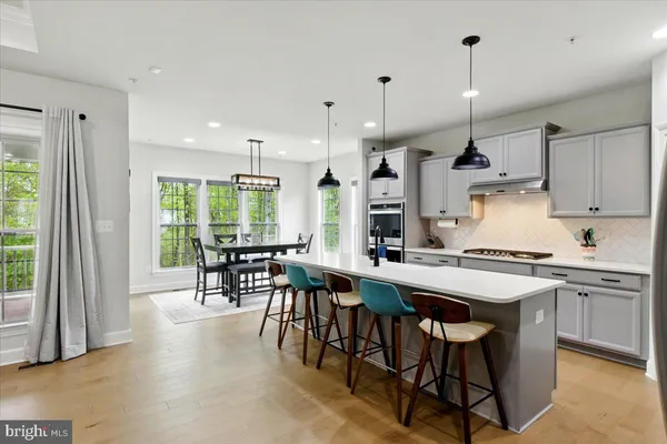 a kitchen with stainless steel appliances granite countertop a stove a refrigerator a kitchen island a dining table and chairs with wooden floor