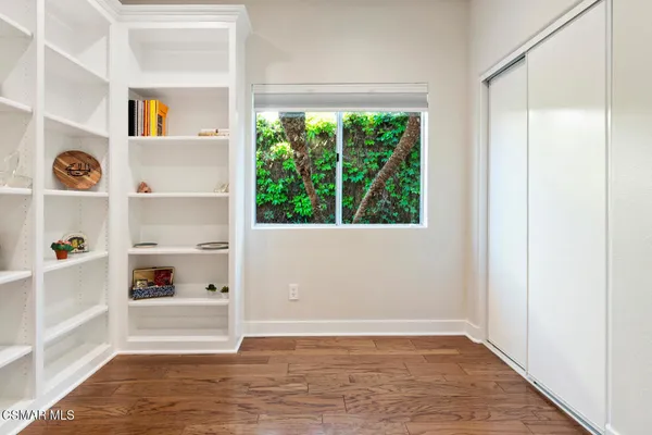 a view of an empty room and kitchen with wooden floor and window