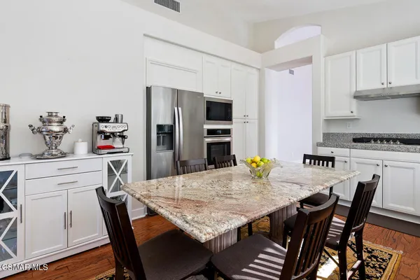 a kitchen with stainless steel appliances granite countertop a dining table chairs and refrigerator