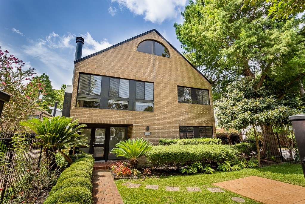 2349 Albans Road, Unit 1 Houston, TX 77005 - Photo 14 of 14 This modern brick home features large windows, offering ample natural light. It's surrounded by lush landscaping and mature trees, providing a serene and private setting.