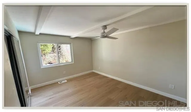 an empty room with wooden floor fan and windows