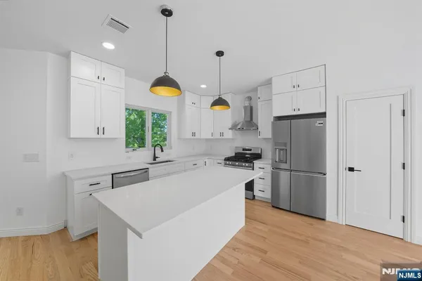 a kitchen with a refrigerator a sink dishwasher and white cabinets with wooden floor