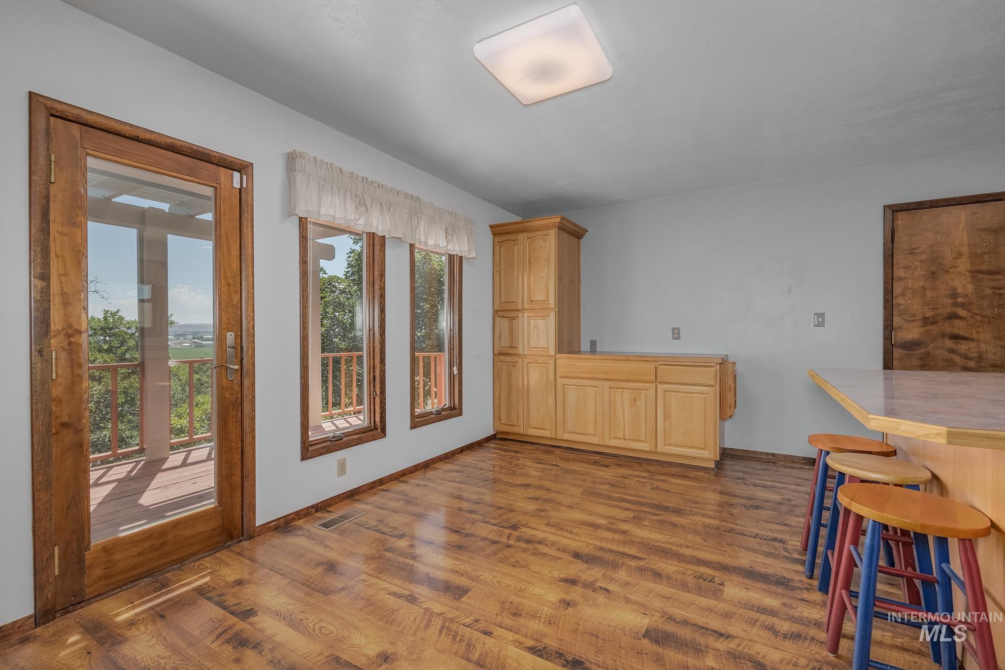 1493 Cove Road Weiser, ID 83672 - Photo 18 of 50 Room with wood-finish flooring, natural wood cabinetry, a built-in breakfast bar, three windows, and a glass-paneled door leading to an outdoor deck