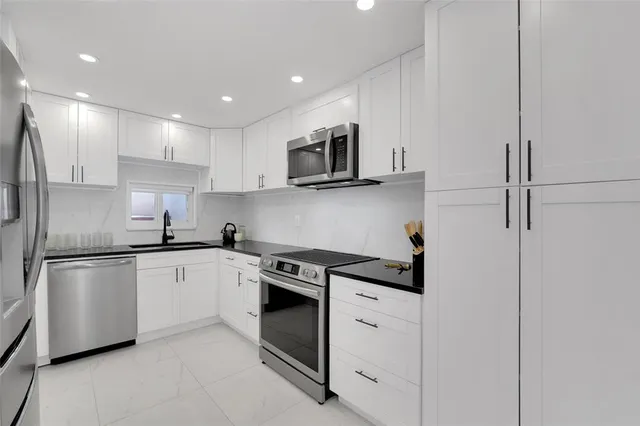 a kitchen with stainless steel appliances granite countertop white cabinets a sink a stove a microwave and a refrigerator