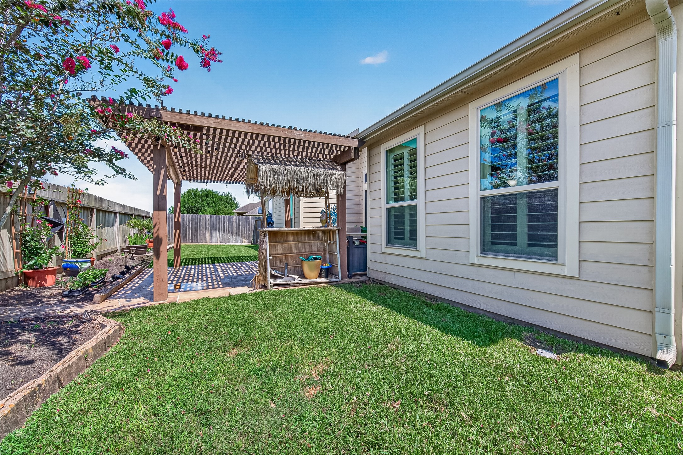 4910 Culver Lane Rosenberg, TX 77471 - Photo 42 of 50 This backyard features a cozy patio with a pergola and a Tiki-style bar, surrounded by a well-maintained lawn and vibrant flower beds, perfect for outdoor relaxation and entertaining.