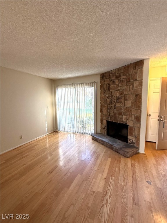 3367 Reka Street Las Vegas, NV 89121 - Photo 6 of 38 Unfurnished living room featuring a textured ceiling, a stone fireplace, and light wood finished floors