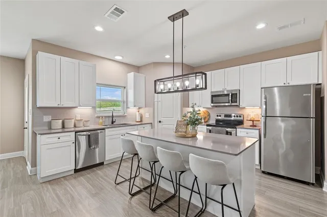 a kitchen with stainless steel appliances kitchen island granite countertop a refrigerator a stove a sink and white cabinets with wooden floor