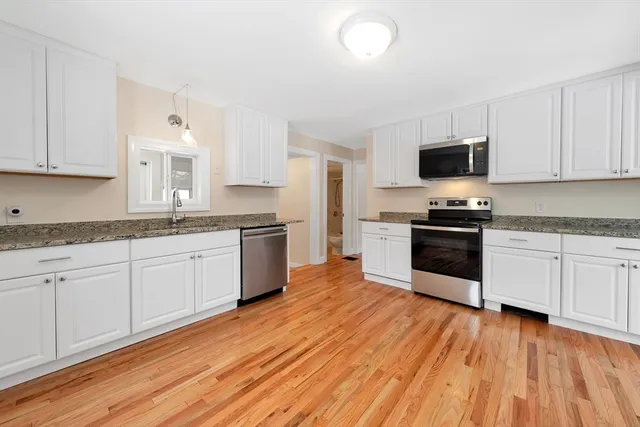 a kitchen with granite countertop a stove top oven a sink dishwasher and a refrigerator with wooden floor