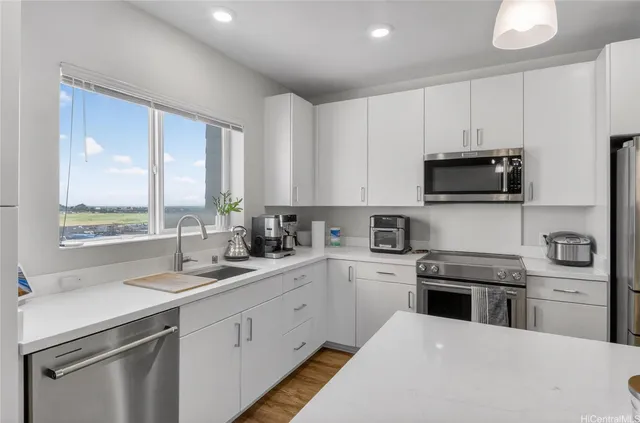 a kitchen with stainless steel appliances a stove a sink a microwave a refrigerator and white cabinets with wooden floor