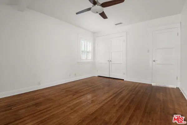 an empty room with wooden floor ceiling fan and windows