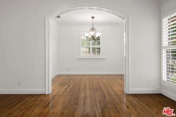 an empty room with wooden floor chandelier and windows