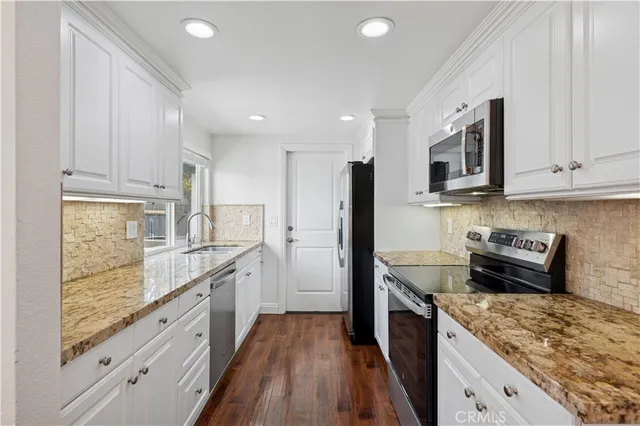 a kitchen with granite countertop kitchen island stainless steel appliances a stove refrigerator sink and cabinets