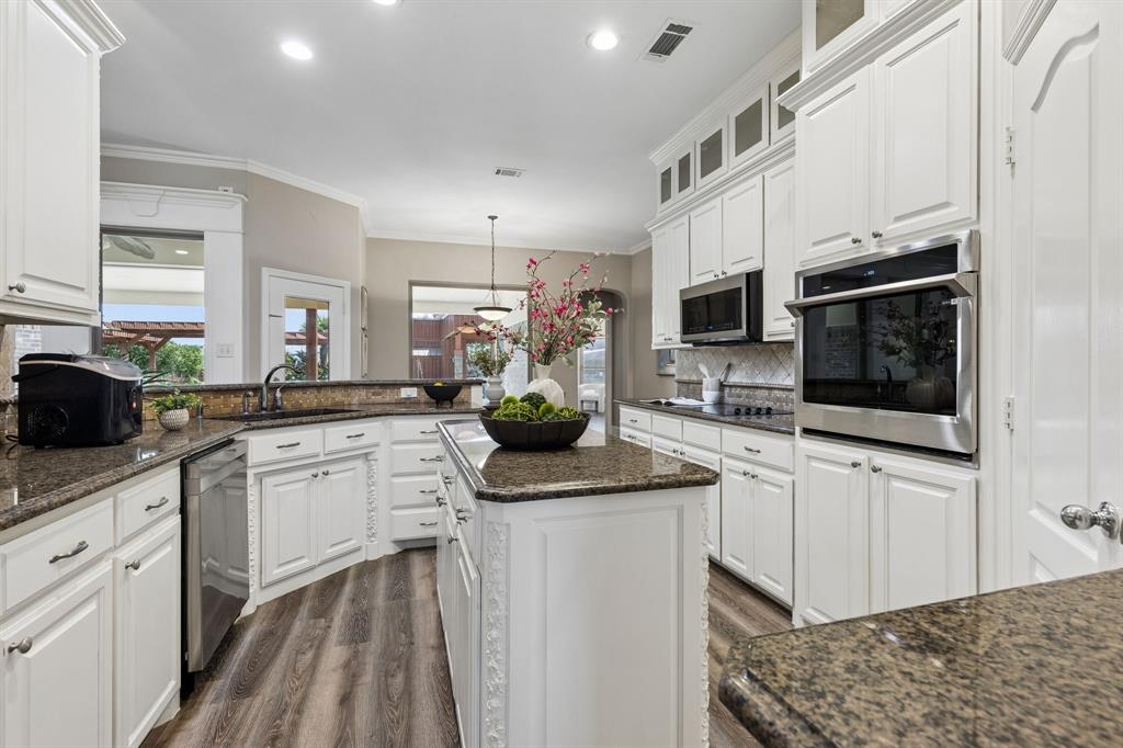 317 Singing Quail Trail Haslet, TX 76052 - Photo 9 of 32 Expansive kitchen featuring white cabinetry, dark stone countertops, wood-finish flooring, a built-in oven, and a central island