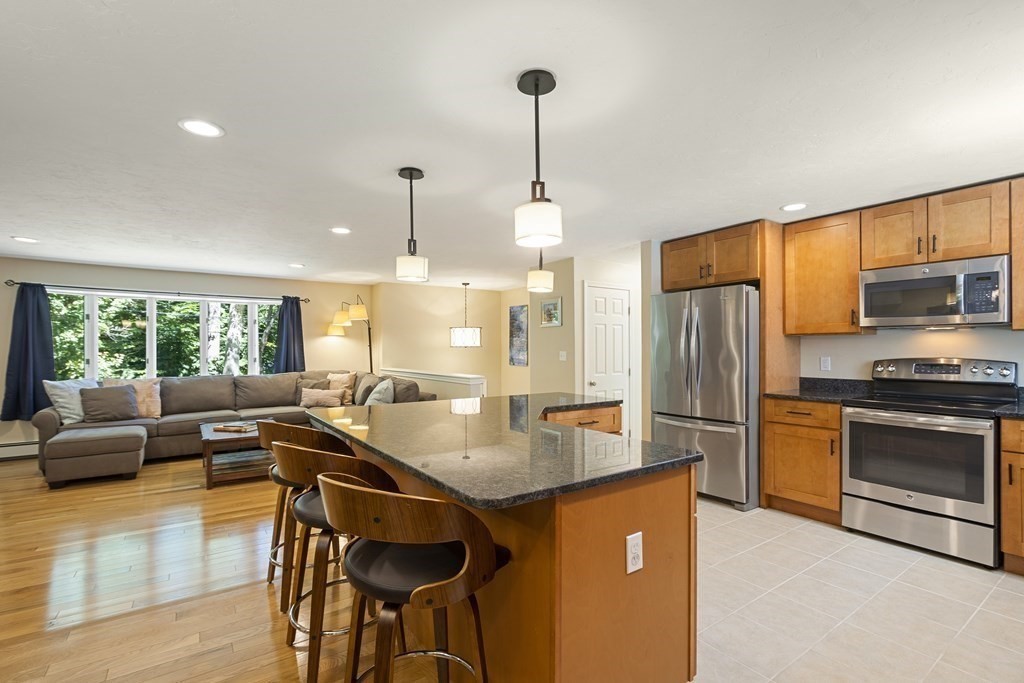 221 Red Acre Road Stow, MA 01775 - Photo 8 of 28 a kitchen with stainless steel appliances granite countertop a stove a refrigerator a microwave a dining table and chairs with wooden floor