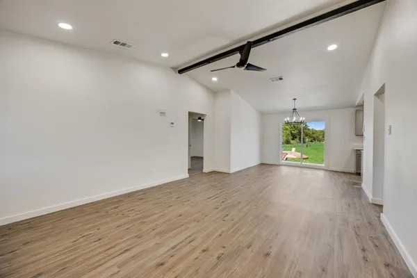 a view of an empty room with wooden floor a ceiling fan and windows