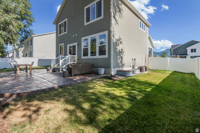 2706 West Maple Street, Unit 285 Mapleton, UT 84664 - Photo 30 of 36 Rear exterior featuring a patterned stamped concrete patio, a white vinyl privacy fence, and an expansive lawn area