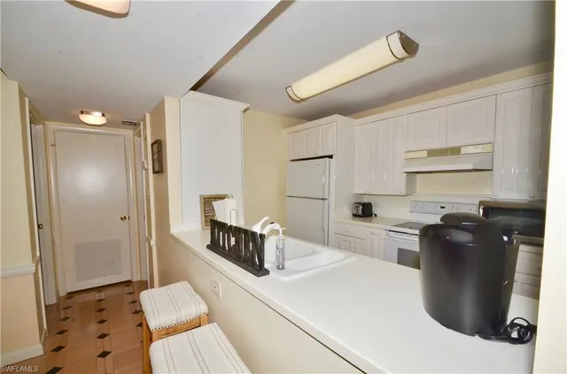 a large white kitchen with a refrigerator a stove a sink dishwasher and a dining table with wooden floor