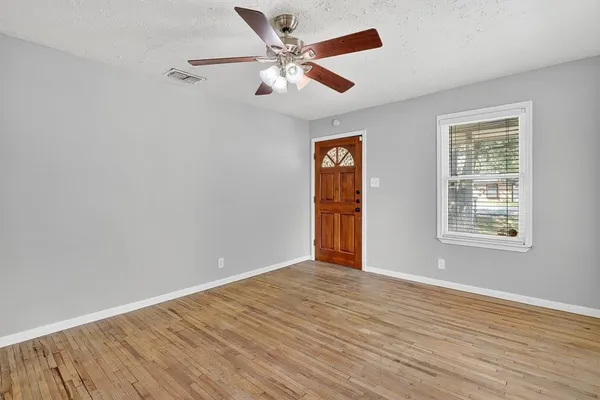 an empty room with wooden floor chandelier fan and windows