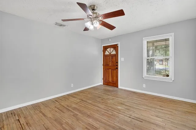 an empty room with wooden floor chandelier fan and windows