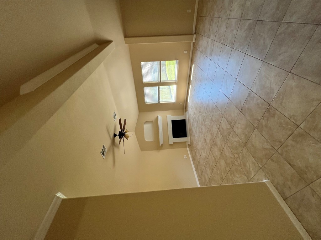 Unfurnished living room featuring baseboards, light tile patterned floors, a ceiling fan, a fireplace with raised hearth, and beam ceiling