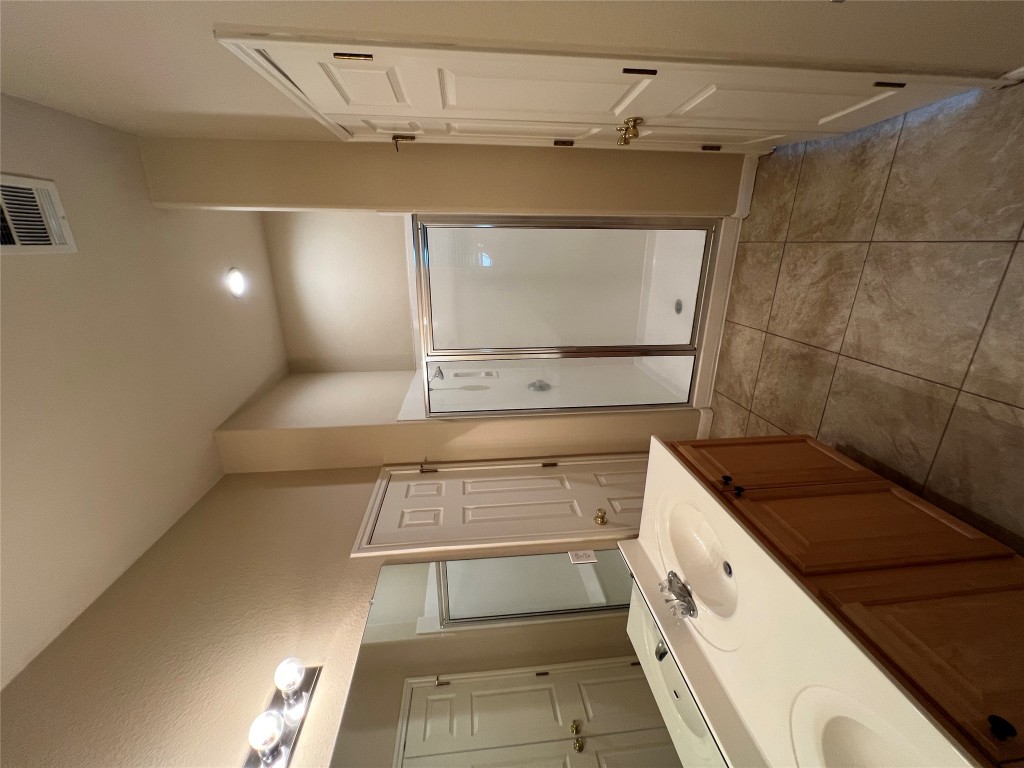 129 Holmstrom Street Hutto, TX 78634 - Photo 14 of 26 Full bathroom featuring double vanity, a stall shower, tile patterned flooring, visible vents, and a sink