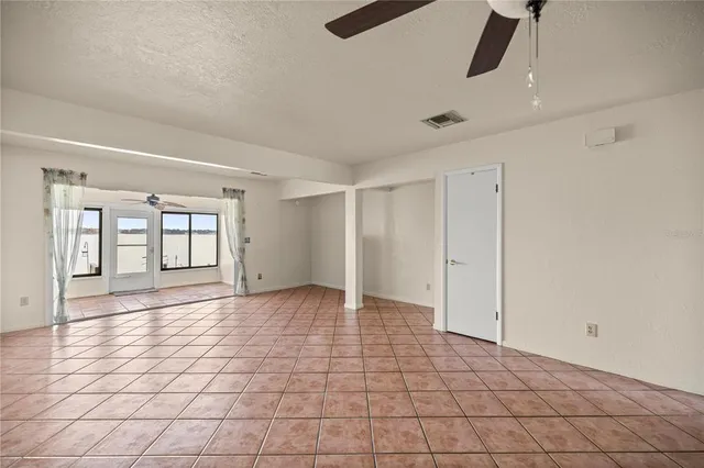 a view of an empty room with window and chandelier fan