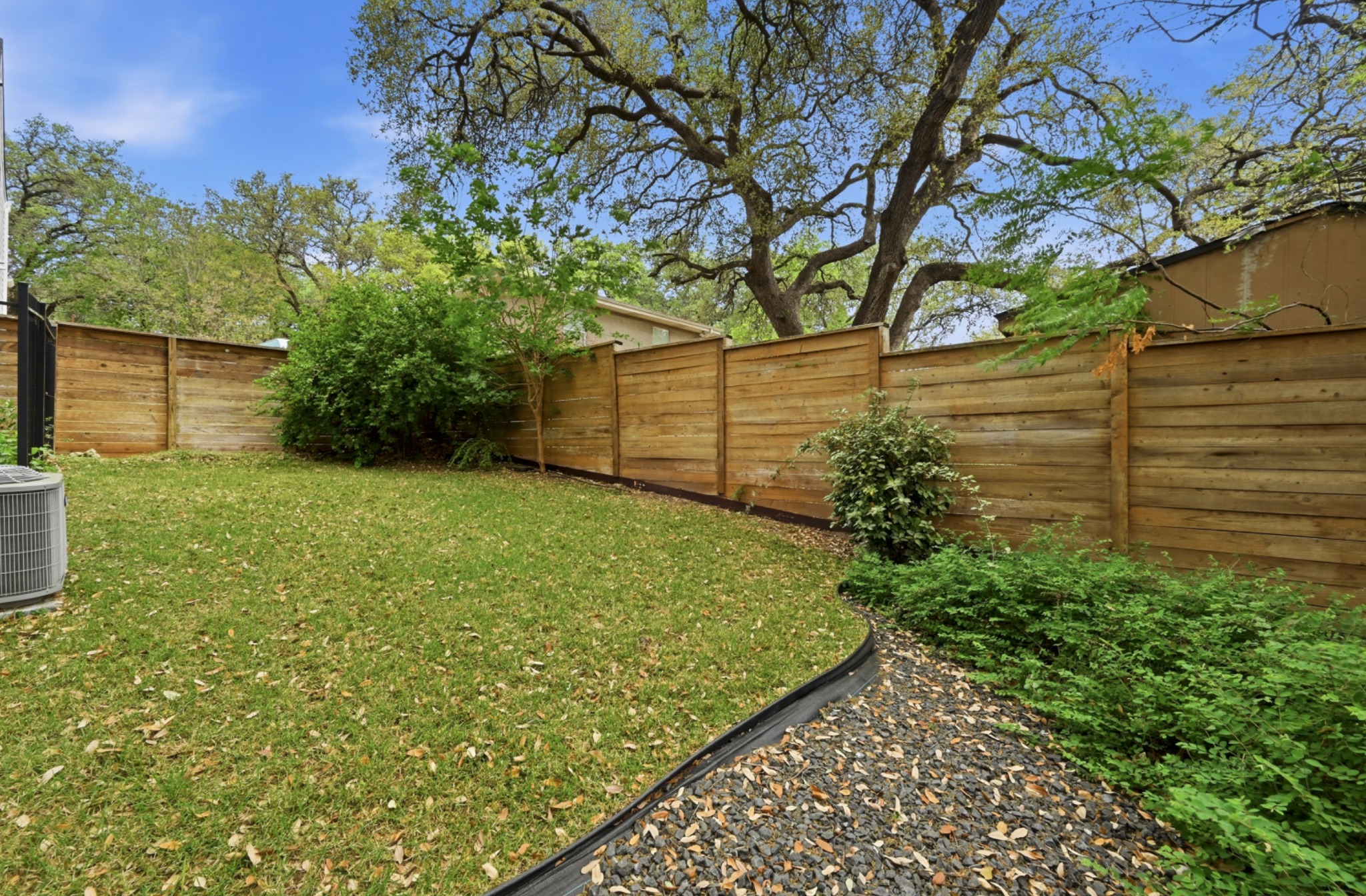 3115 Clawson Road, Unit 201 Austin, TX 78704 - Photo 33 of 34 Private backyard featuring a horizontal plank wood fence, mature perimeter trees, a gravel landscaping bed, and a verdant lawn