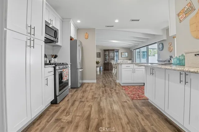 a kitchen with stainless steel appliances granite countertop a refrigerator oven a sink dishwasher and white cabinets with wooden floor