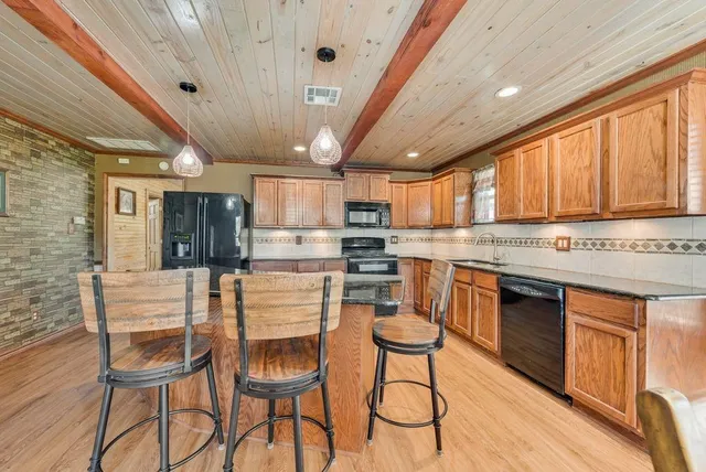 a kitchen with stainless steel appliances granite countertop a stove top oven a sink dishwasher a dining table and chairs with wooden floor