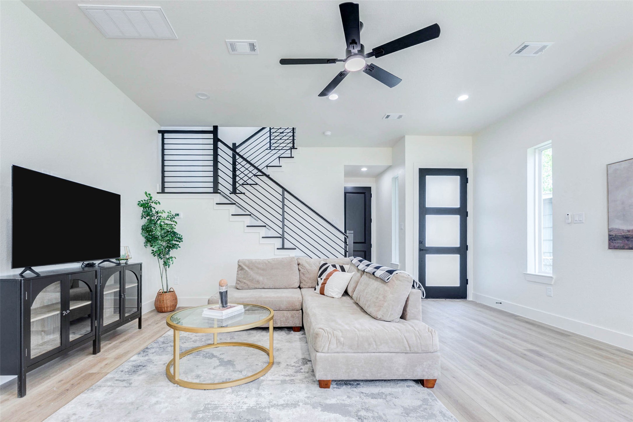 7115 England Street, Unit C Houston, TX 77021 - Photo 12 of 19 The main level features a striking modern staircase with black horizontal metal railings and a frosted-glass accent door.