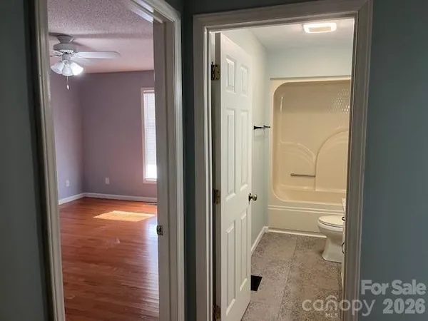 an empty room with wooden floor chandelier fan and windows