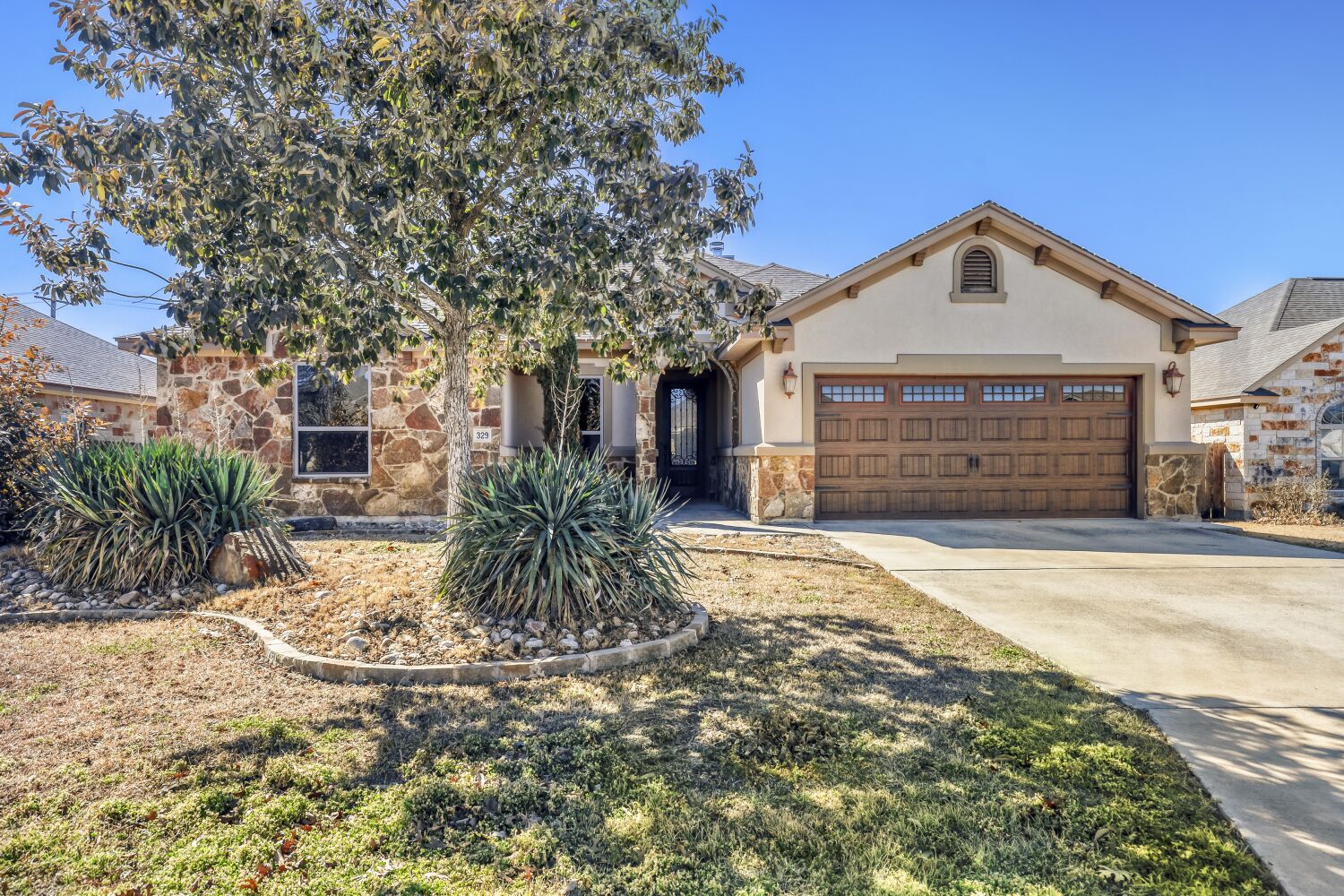 View of front facade featuring stone siding, driveway, an attached garage, and stucco siding